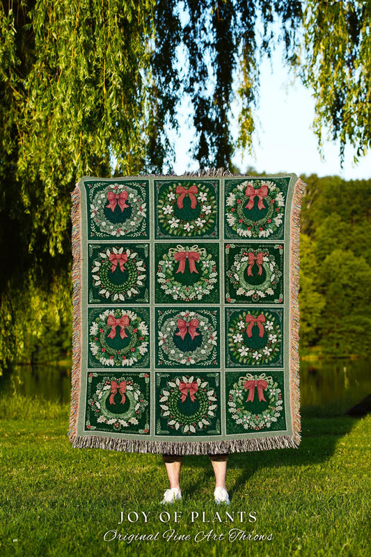 May include: A green woven throw blanket with a repeating pattern of wreaths with red bows. The throw blanket has fringe on the edges. The text 'JOY OF PLANTS Original Fine Art Throws' is printed at the bottom of the image.