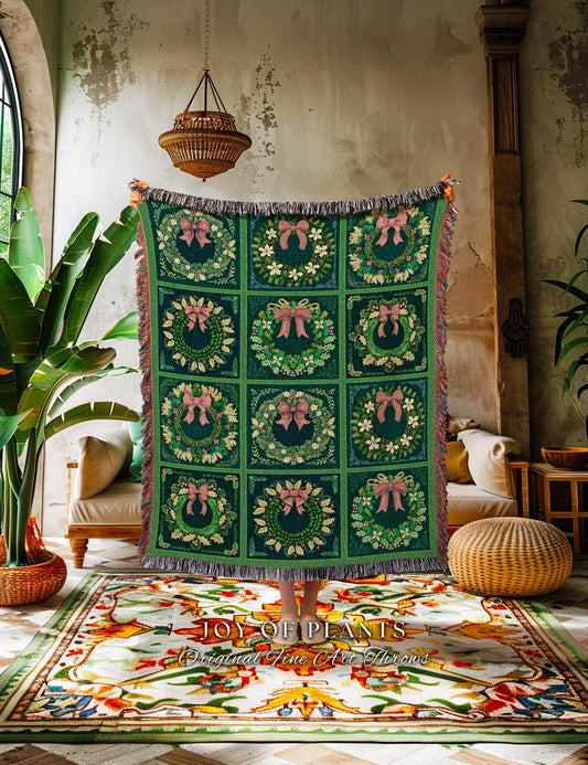 May include: A green woven throw blanket with a fringe border. The blanket features a repeating pattern of wreaths with pink bows. The blanket is displayed on a rug with a colorful floral pattern. The text 'JOY OF PLANTS Original Fine Art Throws' is printed on the rug.