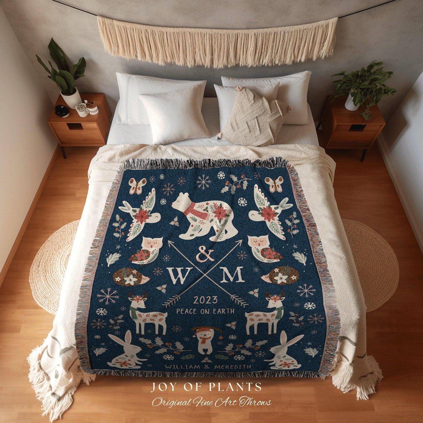 May include: A blue woven throw blanket with a winter holiday theme. The blanket features a white polar bear, a bird, a deer, a rabbit, and an owl. The blanket also features the letters 'W & M' and the text '2023 Peace on Earth William & Meredith Joy of Plants Original Fine Art Throws'.