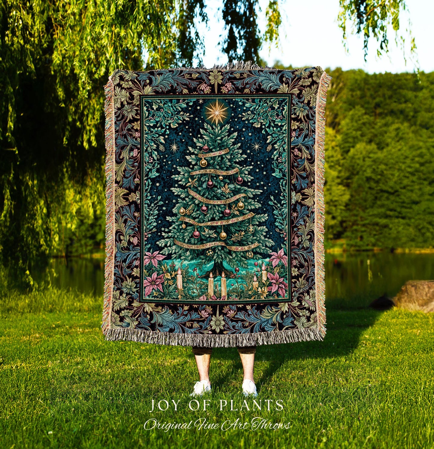 May include: A tapestry throw blanket featuring a Christmas tree design. The tree is green with gold ornaments and ribbons, set against a dark blue background with a star at the top. The border has floral and leaf patterns in shades of blue, green, and pink. The blanket has a fringed edge and the words 'JOY OF PLANTS Original Fine Art Throws' are at the bottom.