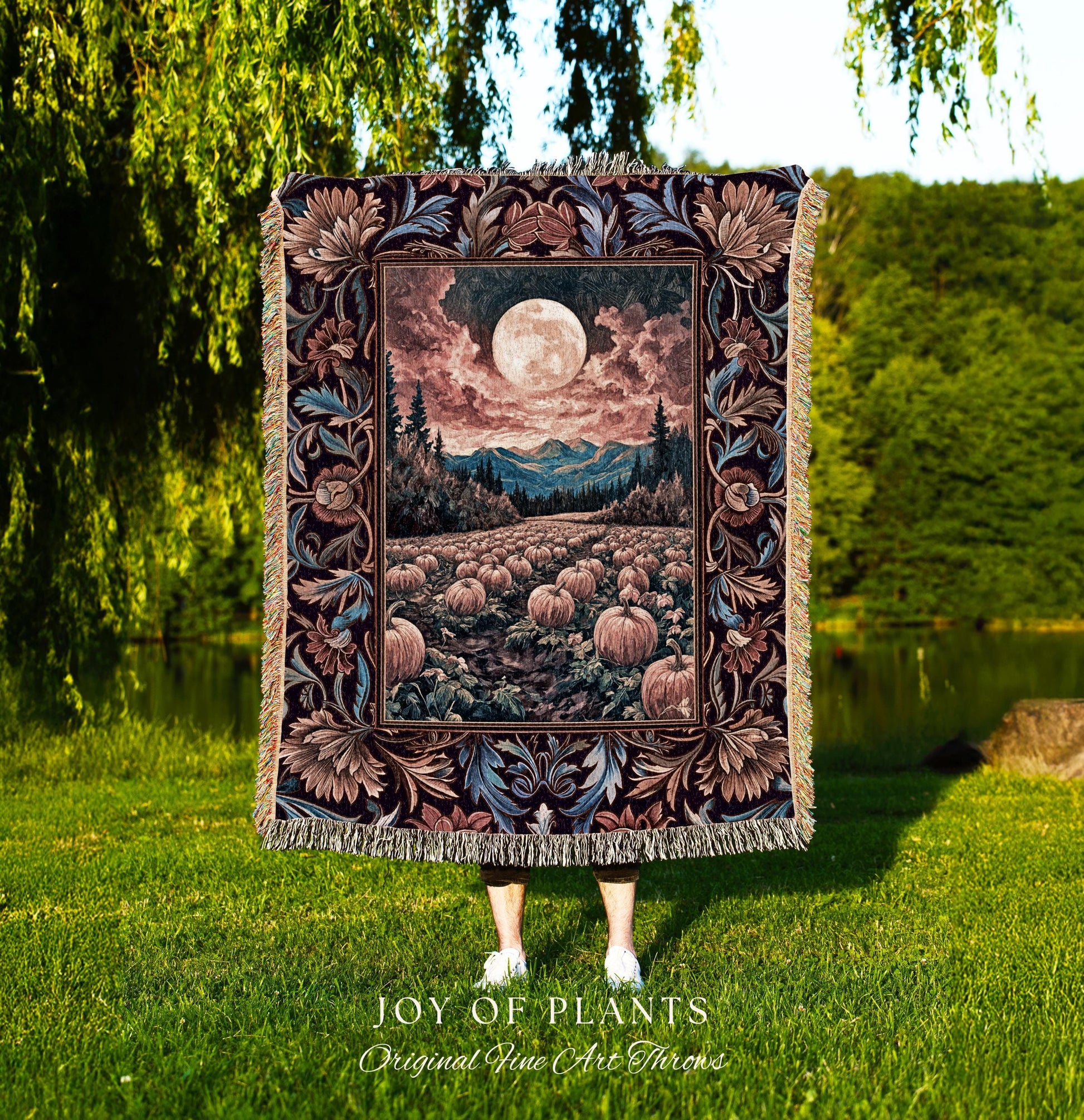 May include: A tapestry throw blanket featuring a full moon over a pumpkin field, mountains, and trees. The blanket has a decorative floral border in shades of brown, blue, and burgundy. The blanket is fringed and the text 'JOY OF PLANTS Original Fine Art Throws' is visible.
