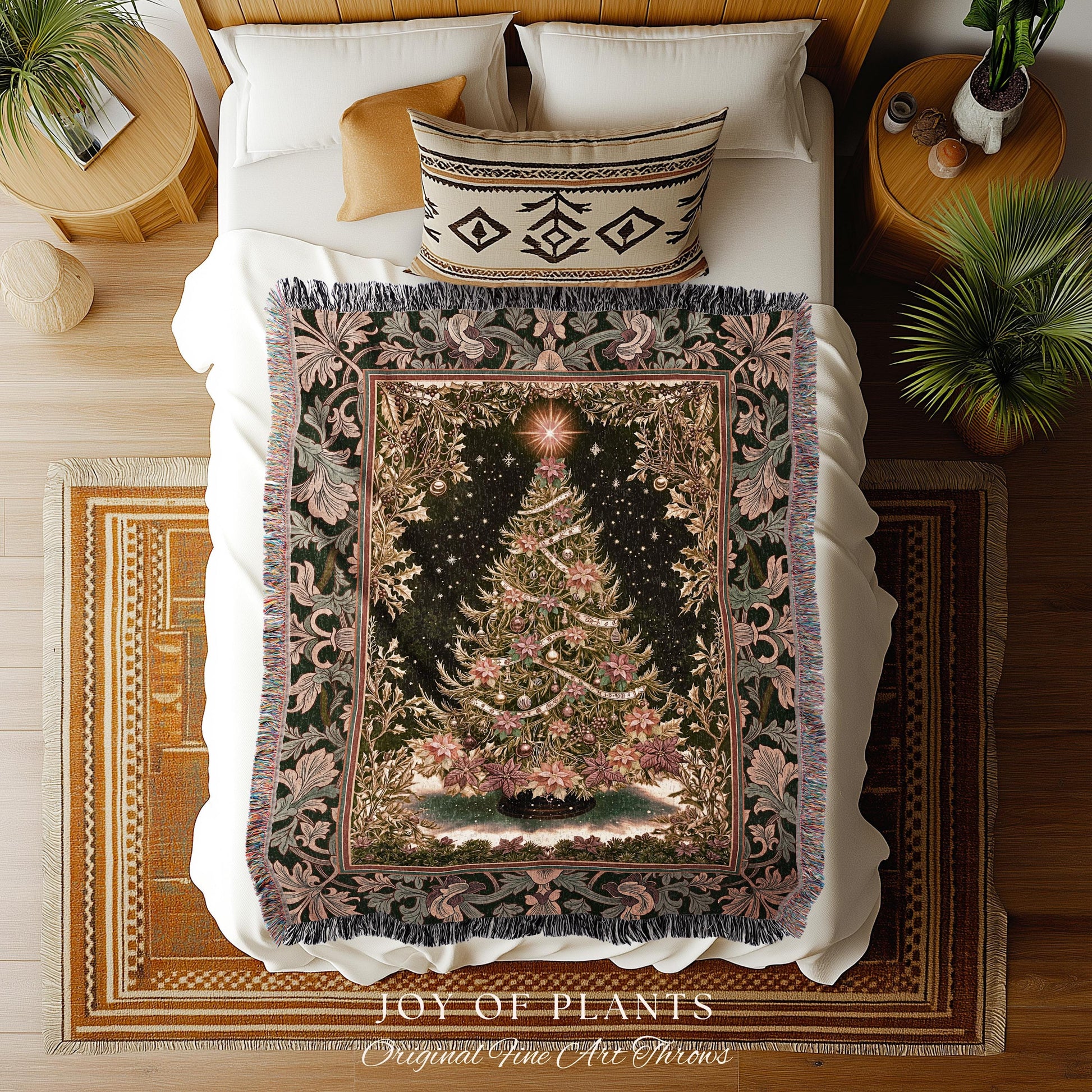 May include: A Christmas tree tapestry throw blanket on a bed. The blanket features a detailed Christmas tree design with ornaments and a star on a dark background. The border has floral and leaf patterns in shades of green and pink. The blanket is fringed and the bed has white sheets and pillows.