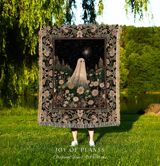 May include: A tapestry throw blanket featuring a night scene with a ghost figure in a field of flowers. The artwork has a black background with a starry sky and a bright star. The ghost is white, and the flowers are in shades of white and yellow. The blanket has a decorative border with floral patterns and the text 'JOY OF PLANTS Original Fine Art Throws'.