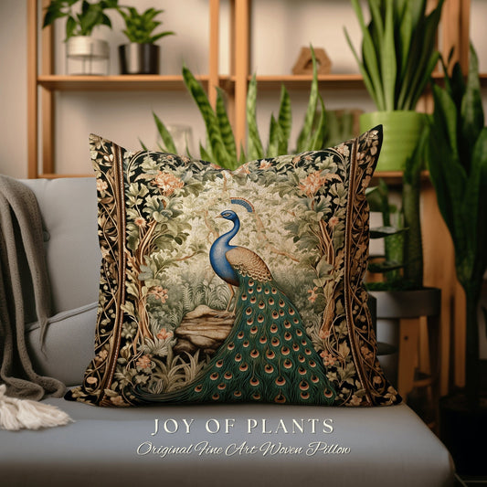 May include: A decorative throw pillow with a woven tapestry design featuring a peacock with a blue head and neck, green and gold tail feathers, and a green and brown leafy background. The pillow is on a gray couch and the text &#39;JOY OF PLANTS Original Fine Art Woven Pillow&#39; is printed below the pillow.