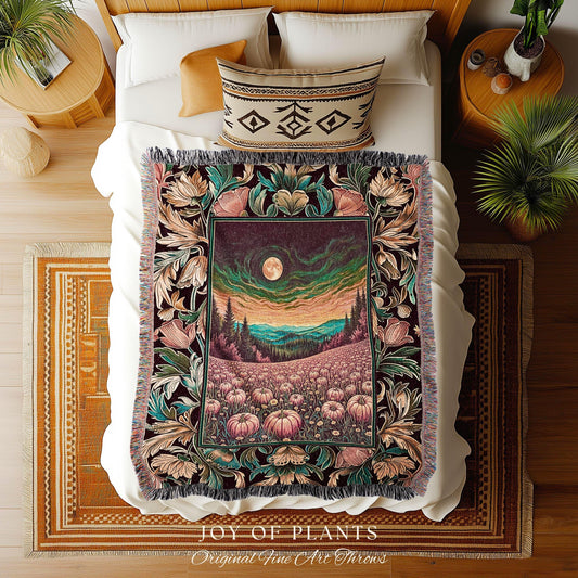 May include: A decorative throw blanket with a floral design. The blanket features a central image of a landscape with a full moon, trees, and a field of pumpkins. The border is adorned with flowers and leaves in shades of teal, pink, and brown. The blanket is on a bed with a white comforter and a patterned pillow.