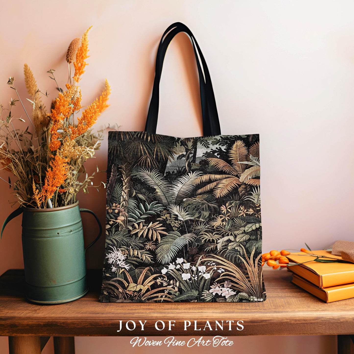 May include: A tote bag with a jungle print design. The bag features a black handle and a detailed illustration of various plants and foliage in shades of green, brown, and white. The words &#39;JOY OF PLANTS&#39; and &#39;Woven Fine Art Tote&#39; are printed at the bottom.