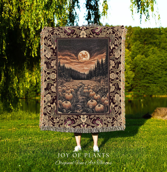 May include: A tapestry throw blanket featuring a nighttime landscape with a full moon, a path lined with pumpkins, and a forest. The border has a floral design with burgundy and tan colors. The blanket is held up in front of a person standing in a grassy area. The text &#39;JOY OF PLANTS Original Fine Art Throws&#39; is at the bottom.