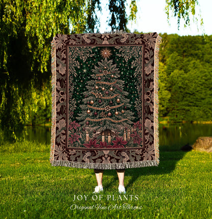 May include: A tapestry throw blanket featuring a detailed Christmas tree design. The tree is adorned with ornaments and candles, set against a dark green background. The blanket has a decorative border with floral and leaf patterns in shades of brown and green. The words &#39;JOY OF PLANTS&#39; and &#39;Original Fine Art Throws&#39; are at the bottom.
