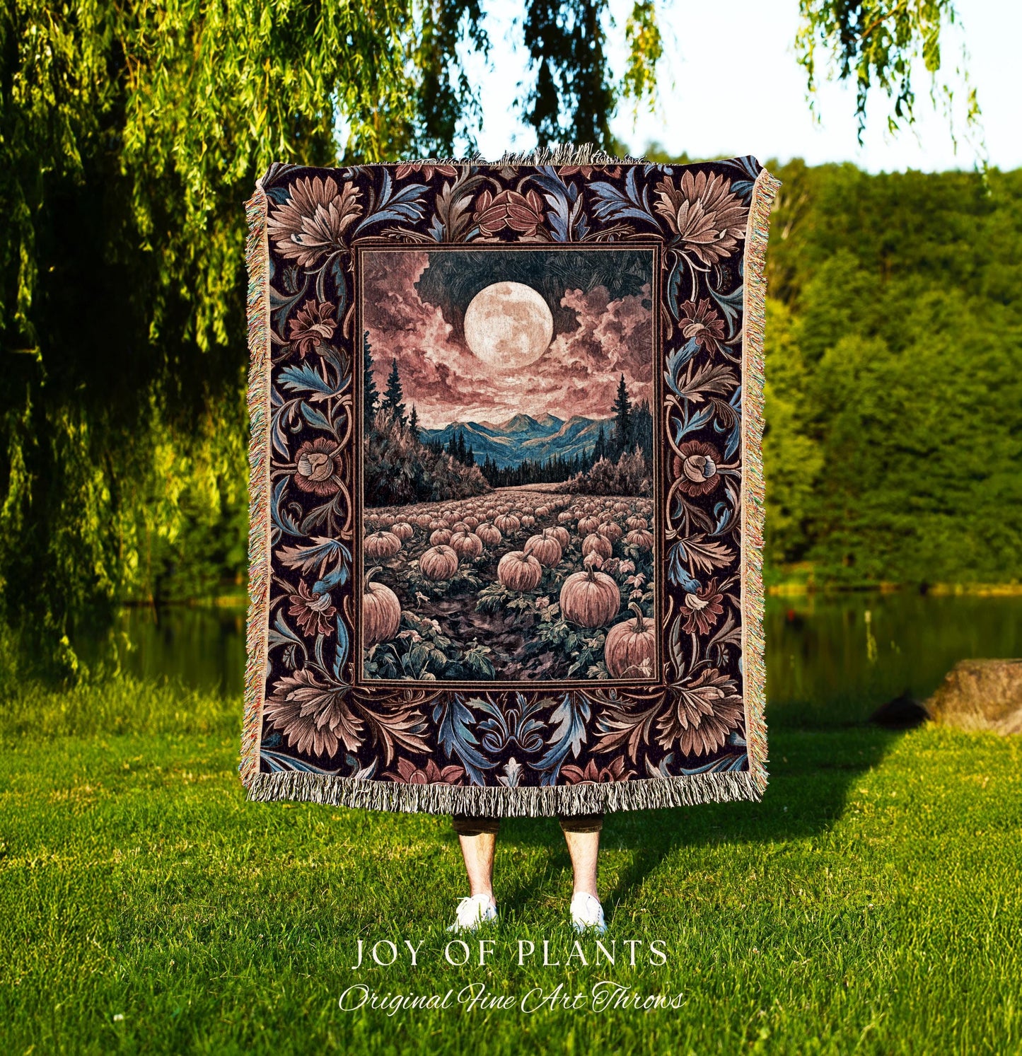 May include: A tapestry throw blanket featuring a full moon over a pumpkin field, mountains, and trees. The blanket has a decorative floral border in shades of brown, blue, and burgundy. The blanket is fringed and the text &#39;JOY OF PLANTS Original Fine Art Throws&#39; is visible.