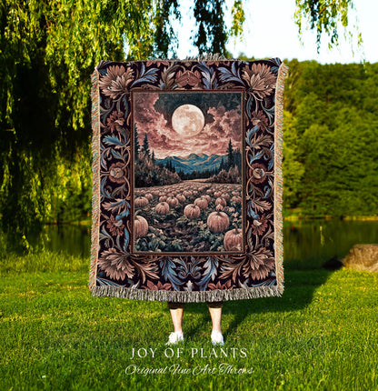 May include: A tapestry throw blanket featuring a full moon over a pumpkin field, mountains, and trees. The blanket has a decorative floral border in shades of brown, blue, and burgundy. The blanket is fringed and the text &#39;JOY OF PLANTS Original Fine Art Throws&#39; is visible.