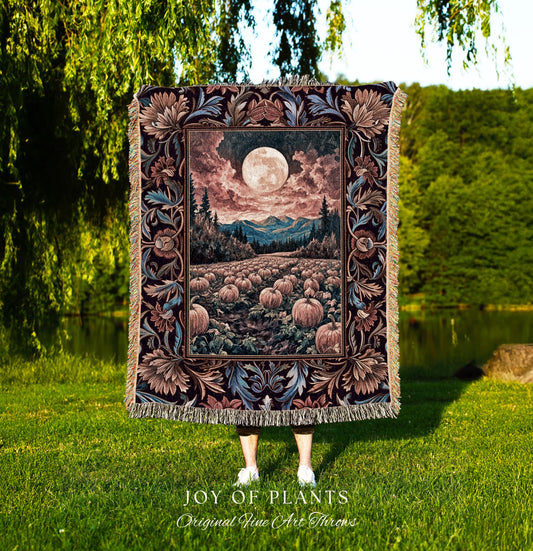 May include: A tapestry throw blanket featuring a full moon over a pumpkin field, mountains, and trees. The blanket has a decorative floral border in shades of brown, blue, and burgundy. The blanket is fringed and the text &#39;JOY OF PLANTS Original Fine Art Throws&#39; is visible.
