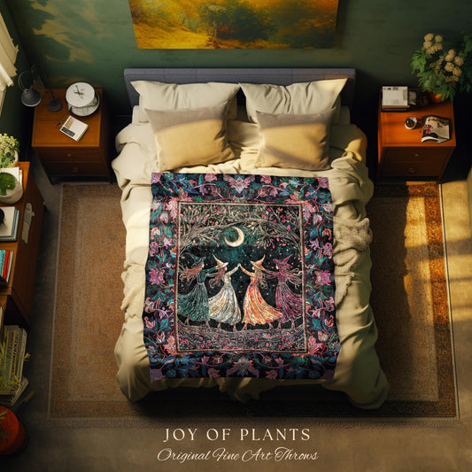May include: A decorative throw blanket with a mystical theme. The blanket features a central design of four figures in flowing dresses dancing under a crescent moon and tree. The border is a dark, floral pattern with shades of blue, purple, and green. The blanket is displayed on a bed.