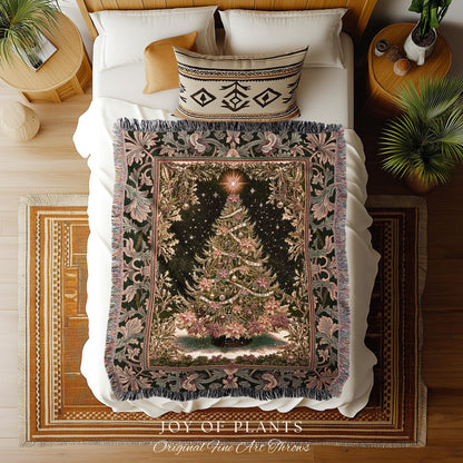 May include: A Christmas tree tapestry throw blanket on a bed. The blanket features a detailed Christmas tree design with ornaments and a star on a dark background. The border has floral and leaf patterns in shades of green and pink. The blanket is fringed and the bed has white sheets and pillows.