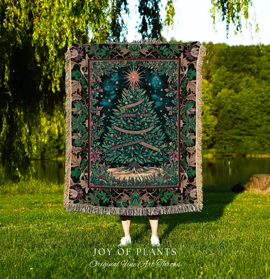 May include: A tapestry throw blanket with a Christmas tree design. The tree is green with a star on top and ribbons with text. The blanket has a dark green background with a floral border in shades of green, pink, and brown. The words 'JOY OF PLANTS Original Fine Art Throws' are at the bottom.
