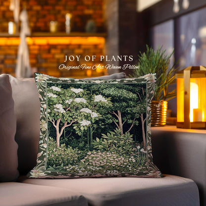 May include: A decorative pillow with a tapestry design featuring a forest scene with trees and white flowers. The pillow is green and white with a brown border. The text "JOY OF PLANTS Original Fine Art Woven Pillow" is printed on the pillow.