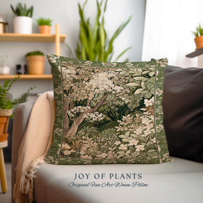 May include: A green throw pillow with a woven tapestry design of a forest scene with white flowers and green leaves. The pillow has the text "JOY OF PLANTS" and "Original Fine Art Woven Pillow" printed on the bottom.