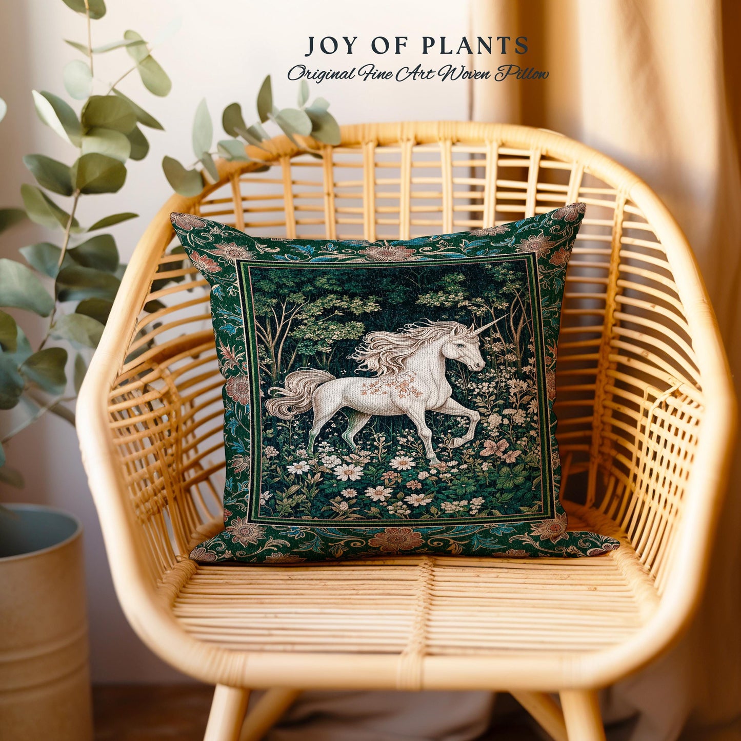 May include: A square decorative pillow with a forest scene featuring a white unicorn. The pillow has a dark green border and is placed on a wicker chair. The text "JOY OF PLANTS Original Fine Art Woven Pillow" is at the top.