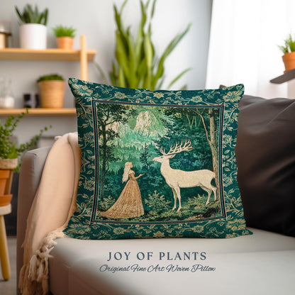 May include: A decorative square pillow with a forest scene featuring a woman and a white deer. The pillow has a dark teal border with floral patterns. The text "JOY OF PLANTS Original Fine Art Woven Pillow" is at the bottom.