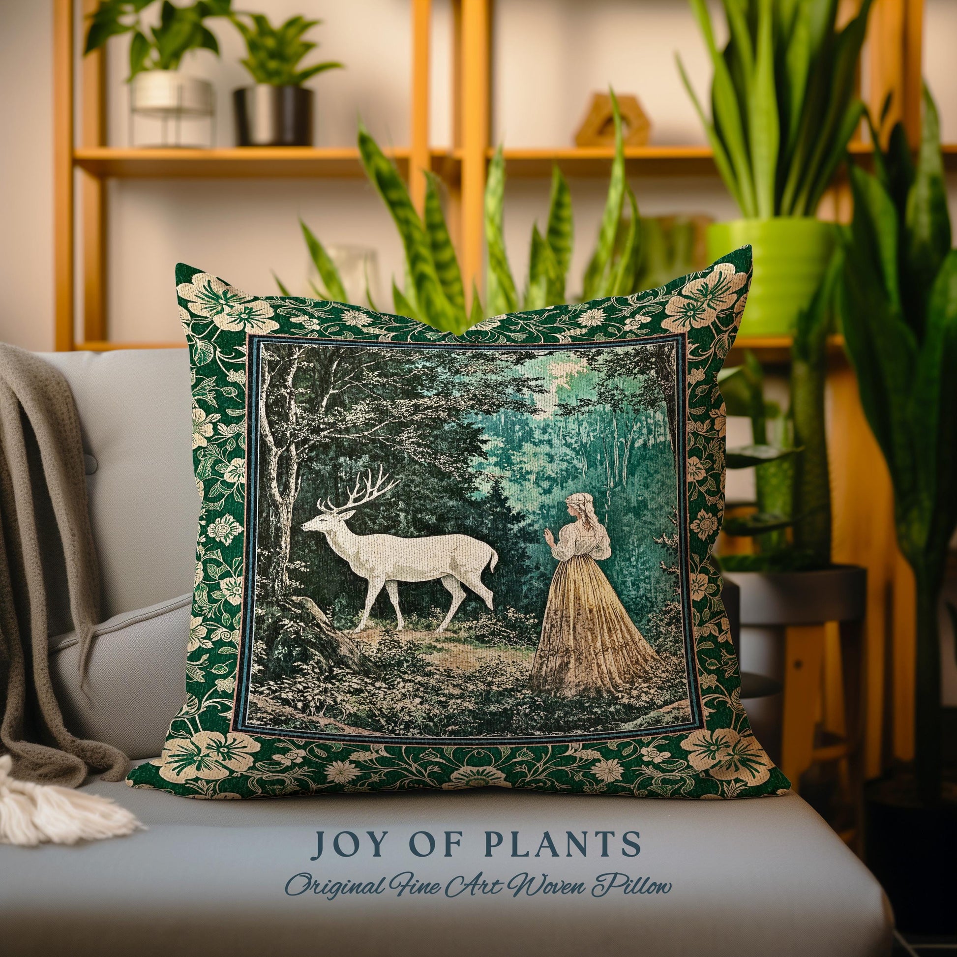 May include: A decorative square pillow with a forest scene featuring a white deer and a woman in a long dress. The pillow has a dark green floral border and the text "JOY OF PLANTS Original Fine Art Woven Pillow".