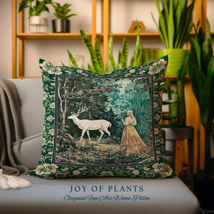 May include: A decorative square pillow with a forest scene featuring a white deer and a woman in a long dress. The pillow has a dark green floral border and the text "JOY OF PLANTS Original Fine Art Woven Pillow".