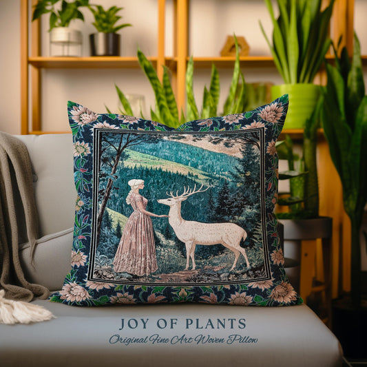 May include: A decorative square pillow with a forest scene featuring a woman and a deer. The pillow has a dark blue floral border and the text "JOY OF PLANTS" and "Original Fine Art Woven Pillow". The pillow is on a gray couch.