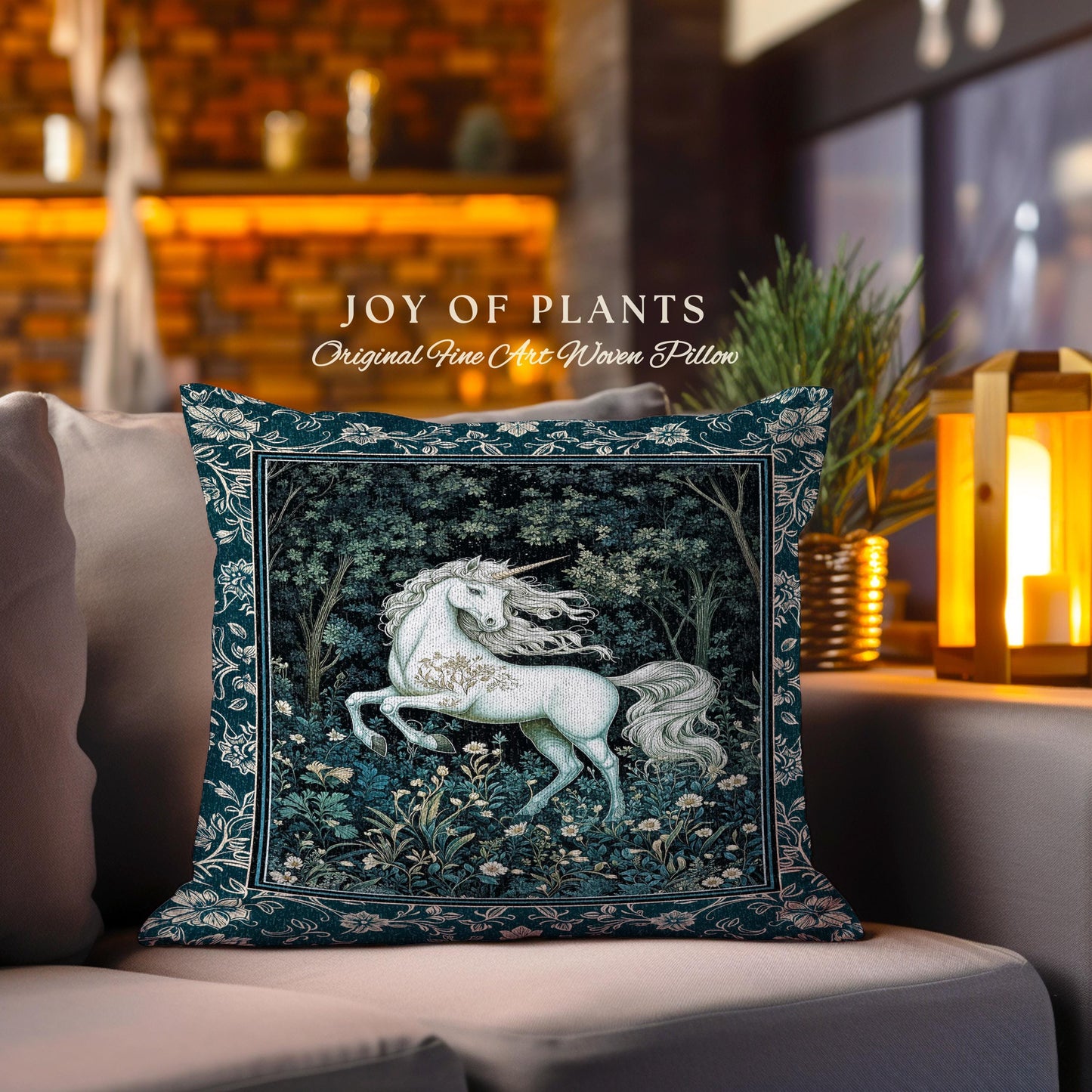 May include: A decorative square pillow with a teal border and a central image of a white unicorn in a forest setting. The pillow has the text "JOY OF PLANTS" and "Original Fine Art Woven Pillow". The pillow is placed on a gray sofa.