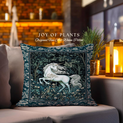 May include: A decorative square pillow with a teal border and a central image of a white unicorn in a forest setting. The pillow has the text "JOY OF PLANTS" and "Original Fine Art Woven Pillow". The pillow is placed on a gray sofa.