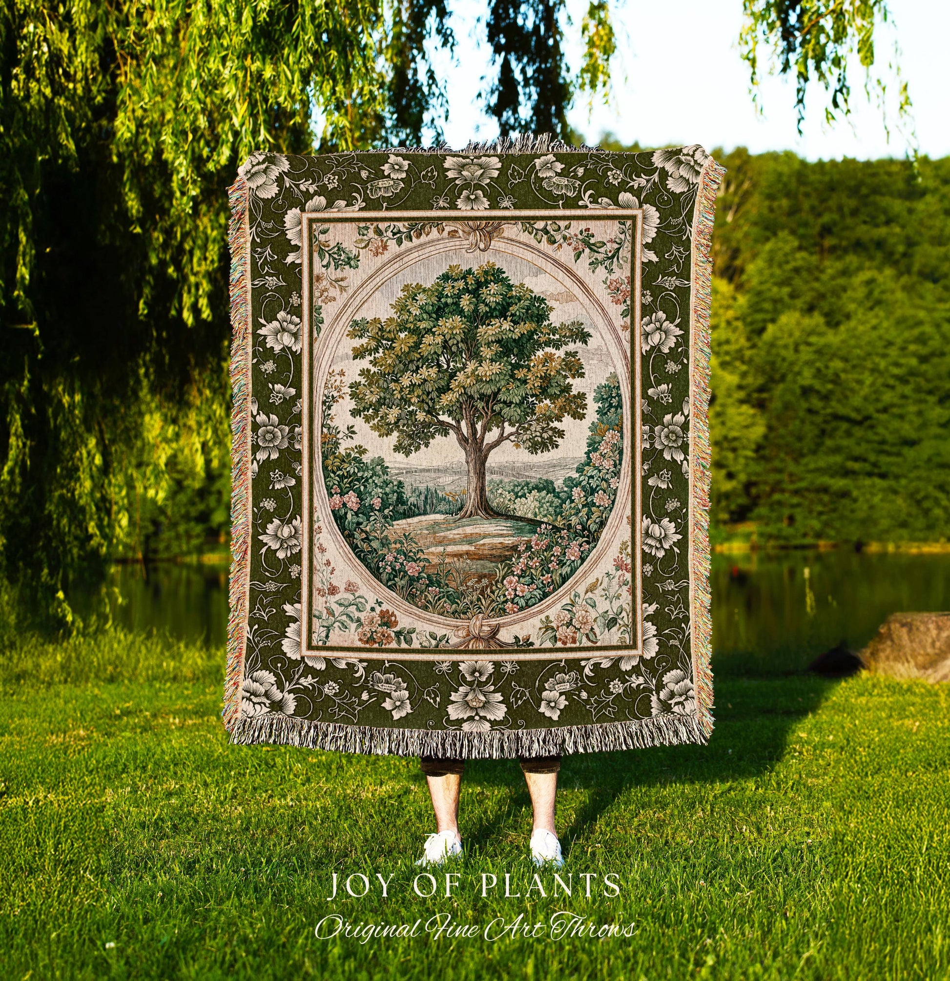 May include: A tapestry throw blanket featuring a detailed tree scene within an oval frame. The blanket has a green floral border and fringe. The text "JOY OF PLANTS Original Fine Art Throws" is at the bottom.