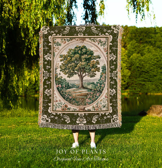 May include: A tapestry throw blanket featuring a detailed tree scene within an oval frame. The blanket has a green floral border and fringe. The text "JOY OF PLANTS Original Fine Art Throws" is at the bottom.