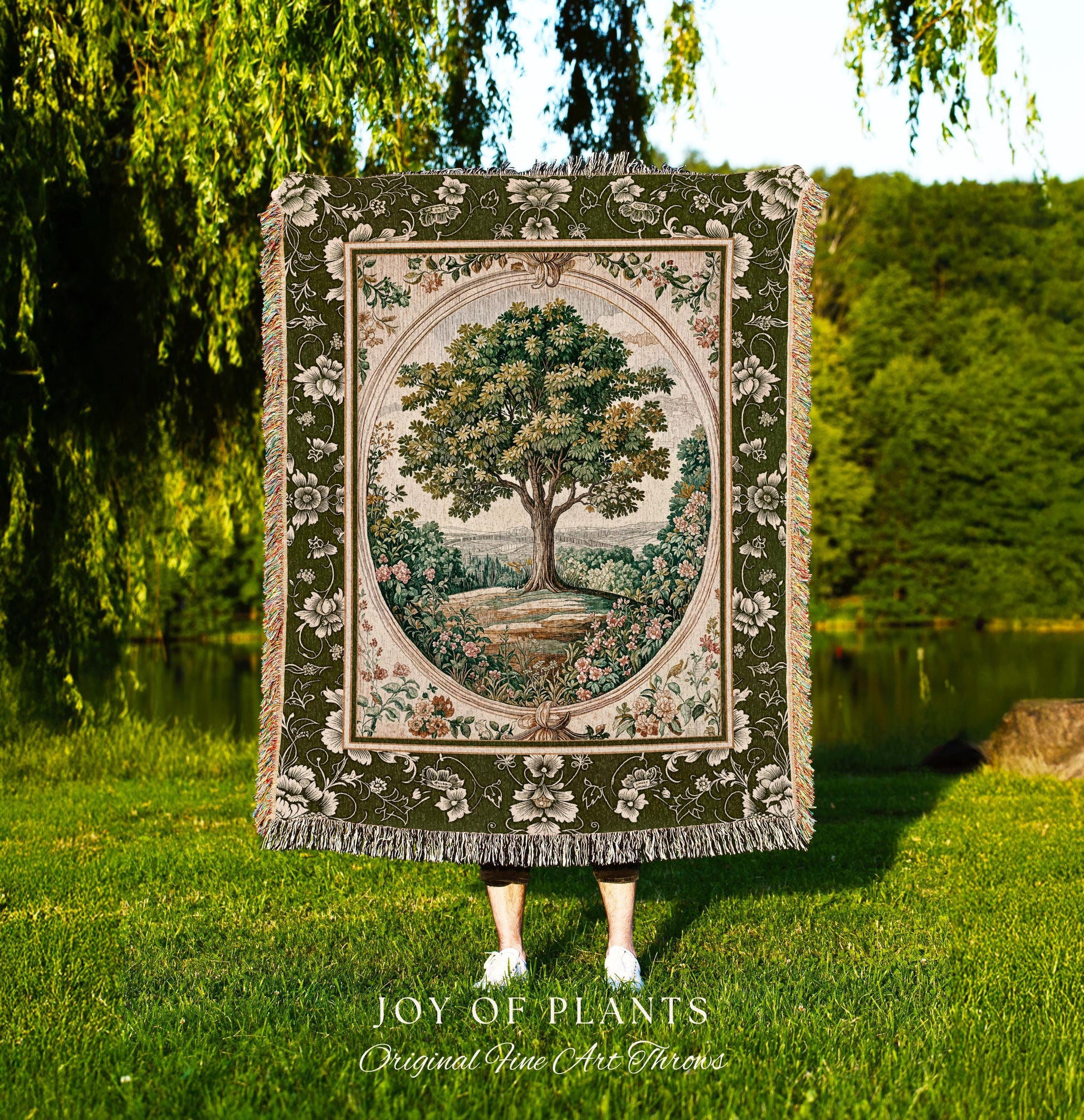 May include: A tapestry throw blanket featuring a detailed tree scene within an oval frame. The blanket has a green floral border and fringe. The text "JOY OF PLANTS Original Fine Art Throws" is at the bottom.