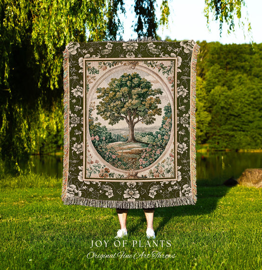May include: A tapestry throw blanket featuring a detailed tree scene within an oval frame. The blanket has a green floral border and fringe. The text "JOY OF PLANTS Original Fine Art Throws" is at the bottom.