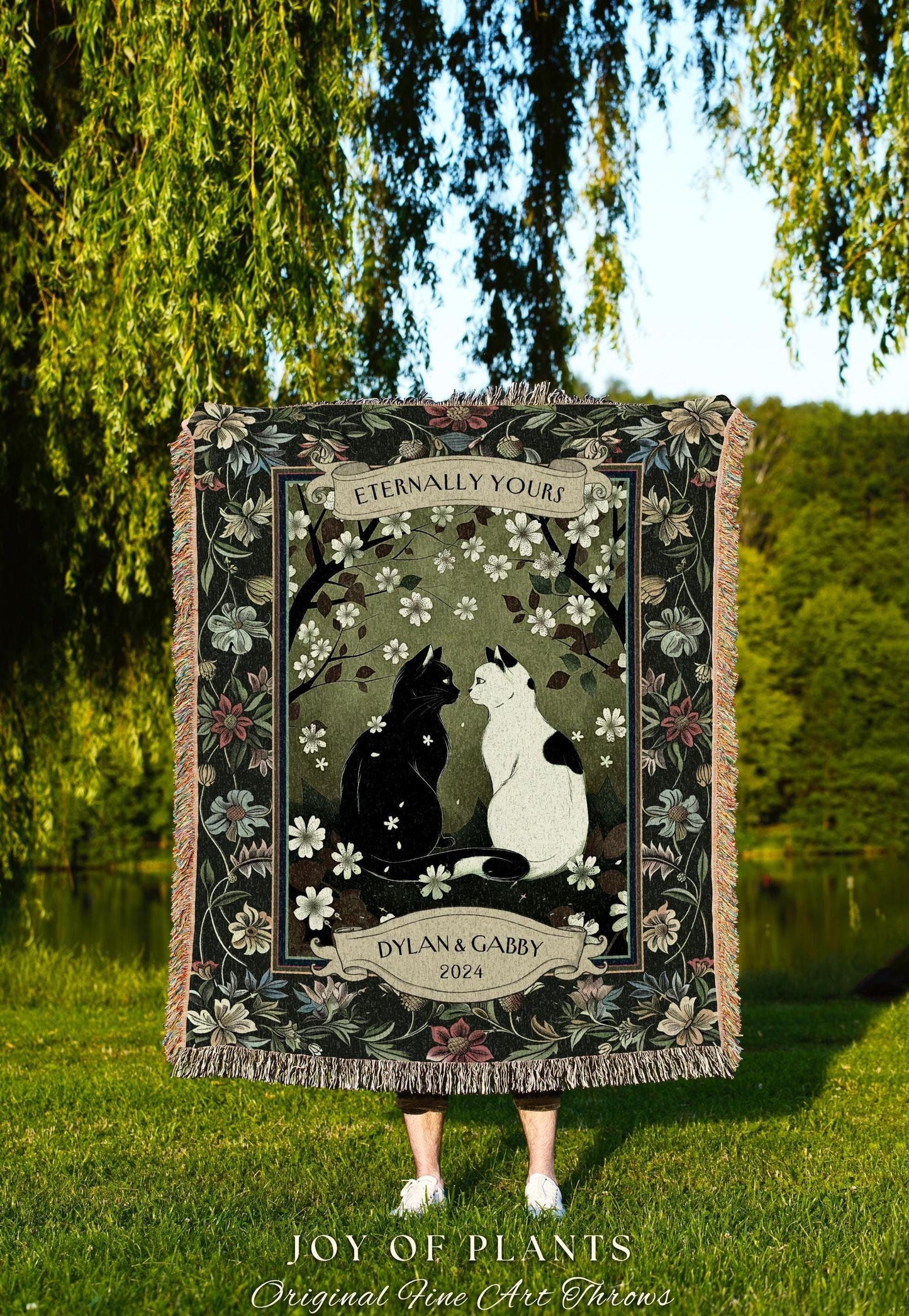 May include: A woven throw blanket featuring a black and white cat illustration under a floral design. The blanket has a dark green border with floral accents and the text "Eternally Yours" and "Dylan & Gabby 2024".