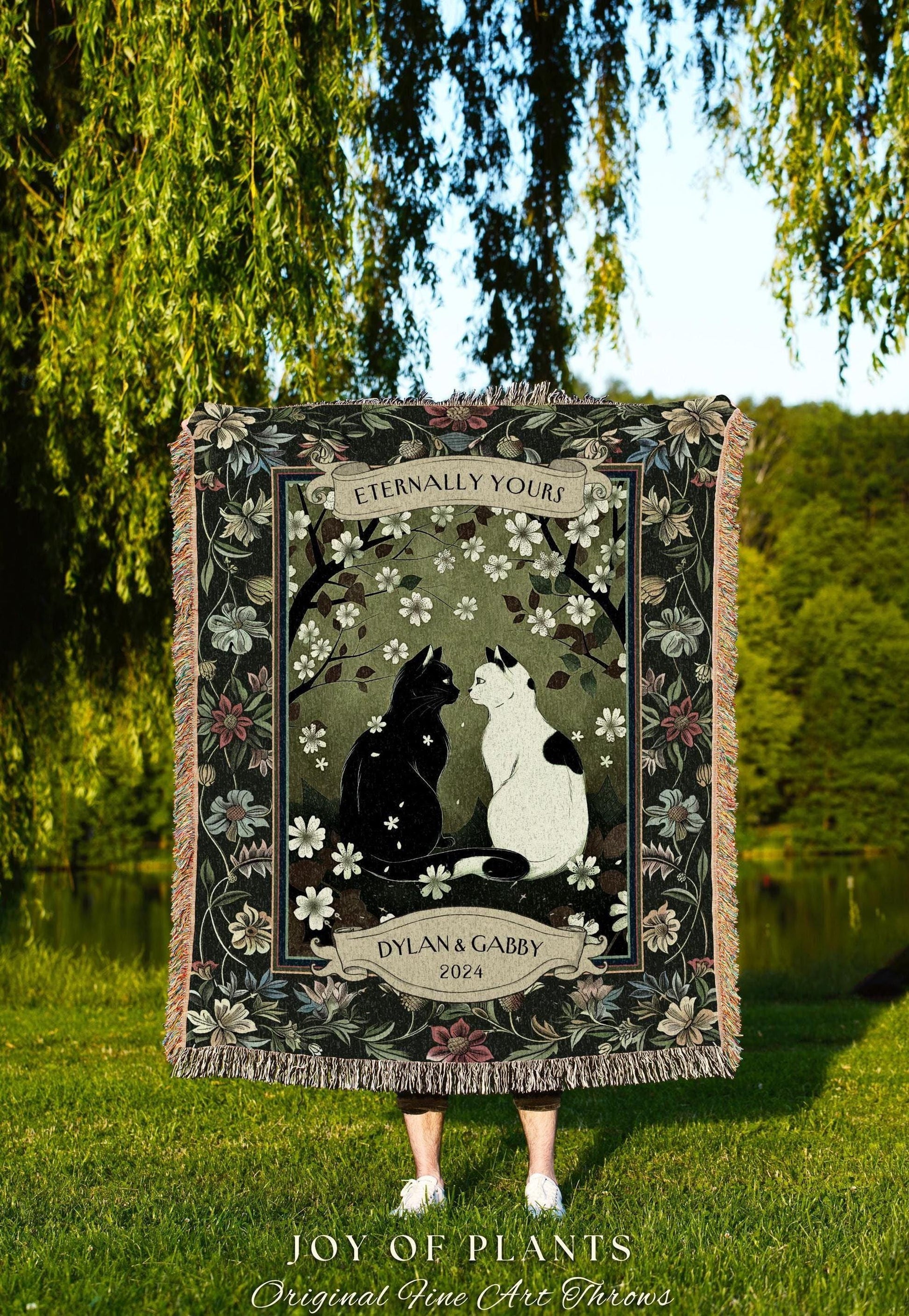 May include: A woven throw blanket featuring a black and white cat illustration under a floral design. The blanket has a dark green border with floral accents and the text "Eternally Yours" and "Dylan & Gabby 2024".