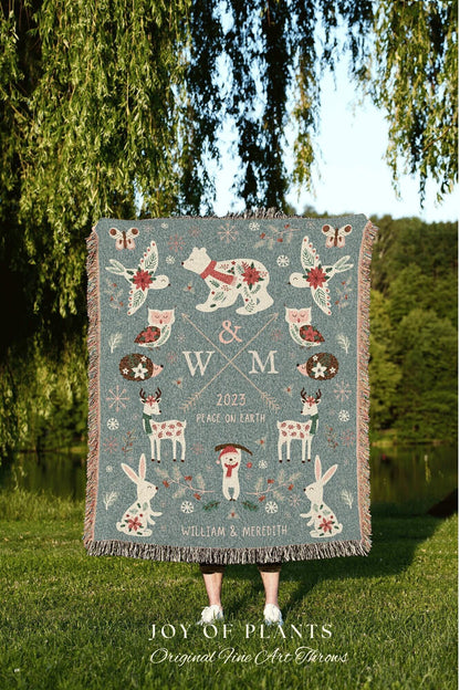 May include: A teal woven throw blanket with a winter holiday theme. The design includes a bear, birds, owls, deer, rabbits, and a snowman. The blanket has a fringe edge and the text "2023 Peace on Earth" and "William & Meredith".
