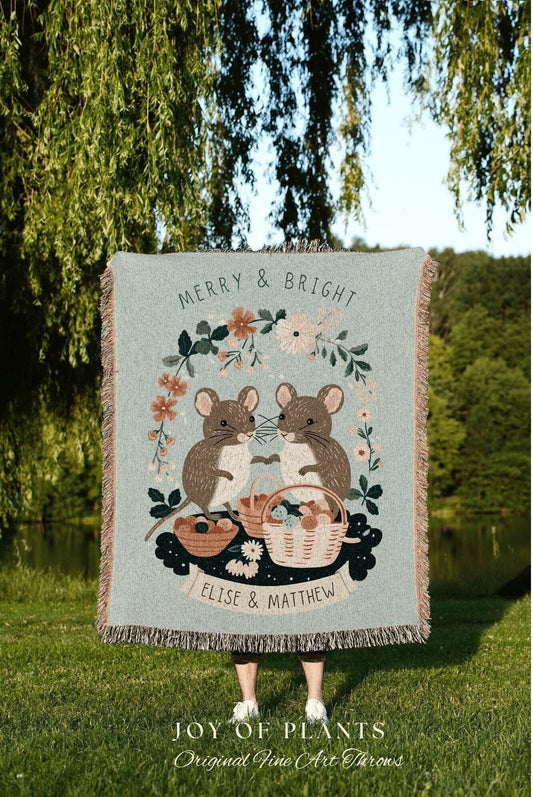 May include: A light blue throw blanket with a whimsical design featuring two brown mice holding hands, surrounded by floral elements and baskets. The text "MERRY & BRIGHT" and "ELISE & MATTHEW" are displayed on the blanket.