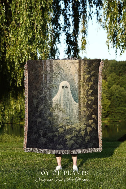 May include: A black throw blanket featuring a ghost in a forest scene. The blanket has a fringed edge and the text "JOY OF PLANTS Original Fine Art Throws" at the bottom. The background shows a lake and trees.