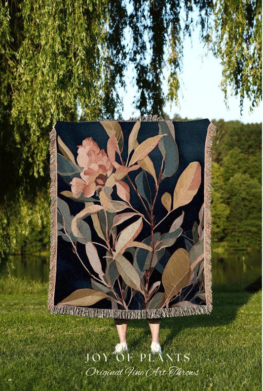 May include: A dark blue throw blanket with a botanical design featuring peach and green leaves and flowers. The blanket has a fringed edge and the text "JOY OF PLANTS Original Fine Art Throws" at the bottom.