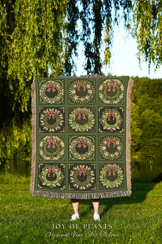 May include: A green woven throw blanket with a fringed border. The blanket features a repeating pattern of nine green wreaths with red bows. The text 'JOY OF PLANTS Original Fine Art Throws' is printed below the blanket.