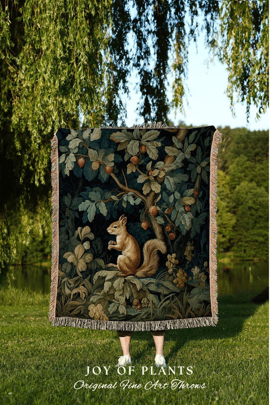 May include: A tapestry throw blanket featuring a detailed illustration of a squirrel in a forest setting. The artwork includes a squirrel, trees, and foliage in shades of brown, green, and blue. The blanket has a fringed edge and the text "JOY OF PLANTS Original Fine Art Throws".