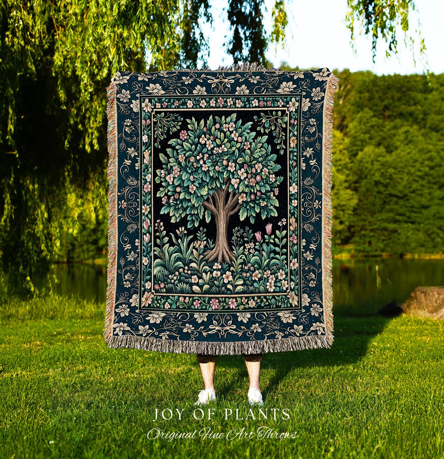 May include: A tapestry throw featuring a detailed tree design with pink and white blossoms, set against a black background. The throw has a dark teal border with floral patterns and fringe. The text "JOY OF PLANTS Original Fine Art Throws" is at the bottom.