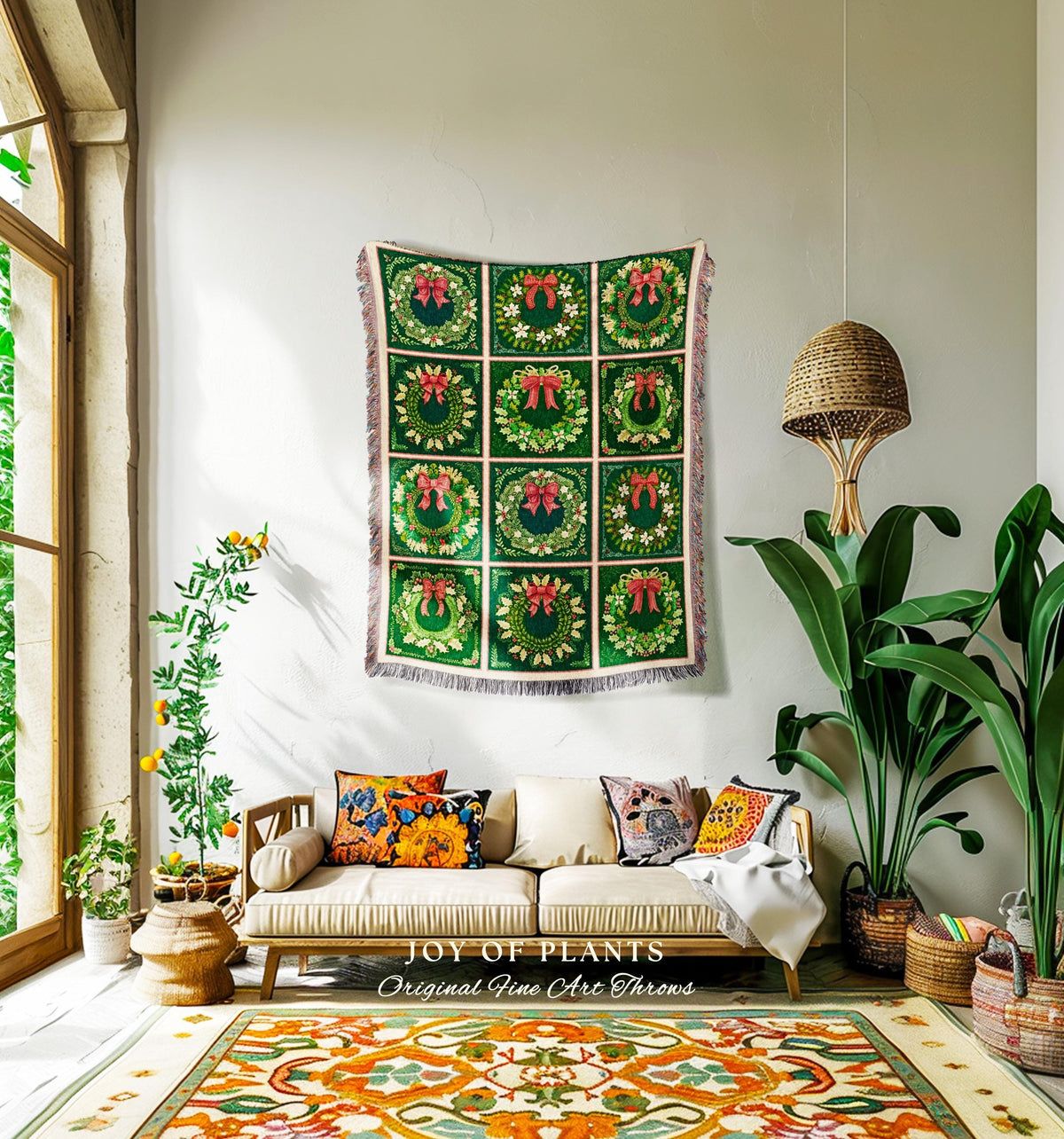 May include: A green throw blanket with a repeating pattern of green wreaths with red bows. The blanket is hanging on a white wall above a light brown couch with white cushions and colorful throw pillows. The couch is in a living room with a green plant in a brown pot and a woven light fixture hanging from the ceiling. The rug on the floor is a cream, orange, and green pattern. The text on the blanket reads 'Joy of Plants Original Fine Art Throws'.