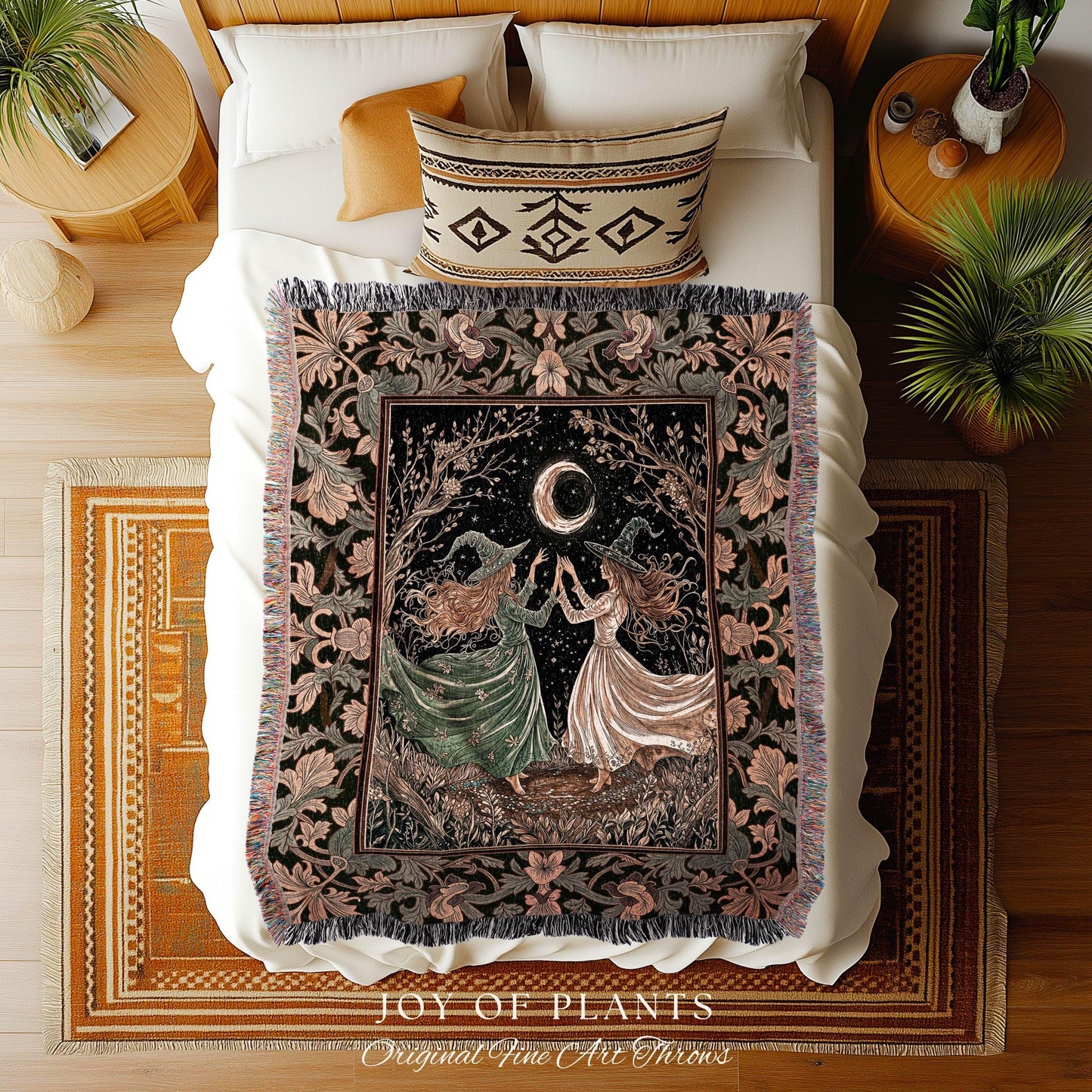 May include: A tapestry throw blanket featuring a mystical scene with two figures under a crescent moon. The blanket has a black background with a floral border in shades of pink and green. The figures are wearing witch hats and dresses. The text 'JOY OF PLANTS Original Fine Art Throws' is at the bottom.