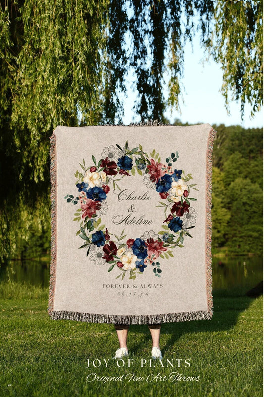 May include: A beige throw blanket with a floral wreath design in burgundy, navy, and cream colors. The text "Charlie & Adeline" and "Forever & Always 09.17.24" are displayed within the wreath. The blanket has a fringed edge.