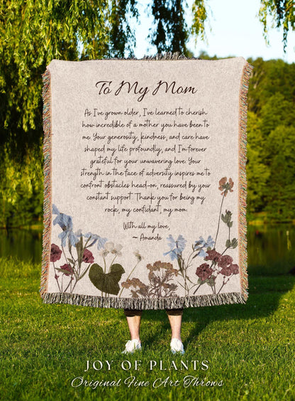 May include: A beige throw blanket with floral accents and the text "To My Mom." The blanket features a floral design with blue, burgundy, and brown flowers. The bottom of the blanket has a fringe.
