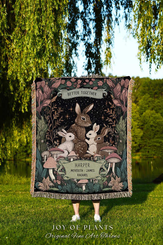 May include: A woven throw blanket featuring a family of rabbits under a starry night sky. The blanket has a fringe border and includes the text "Better Together" and names. The bottom of the blanket reads "JOY OF PLANTS Original Fine Art Throws."