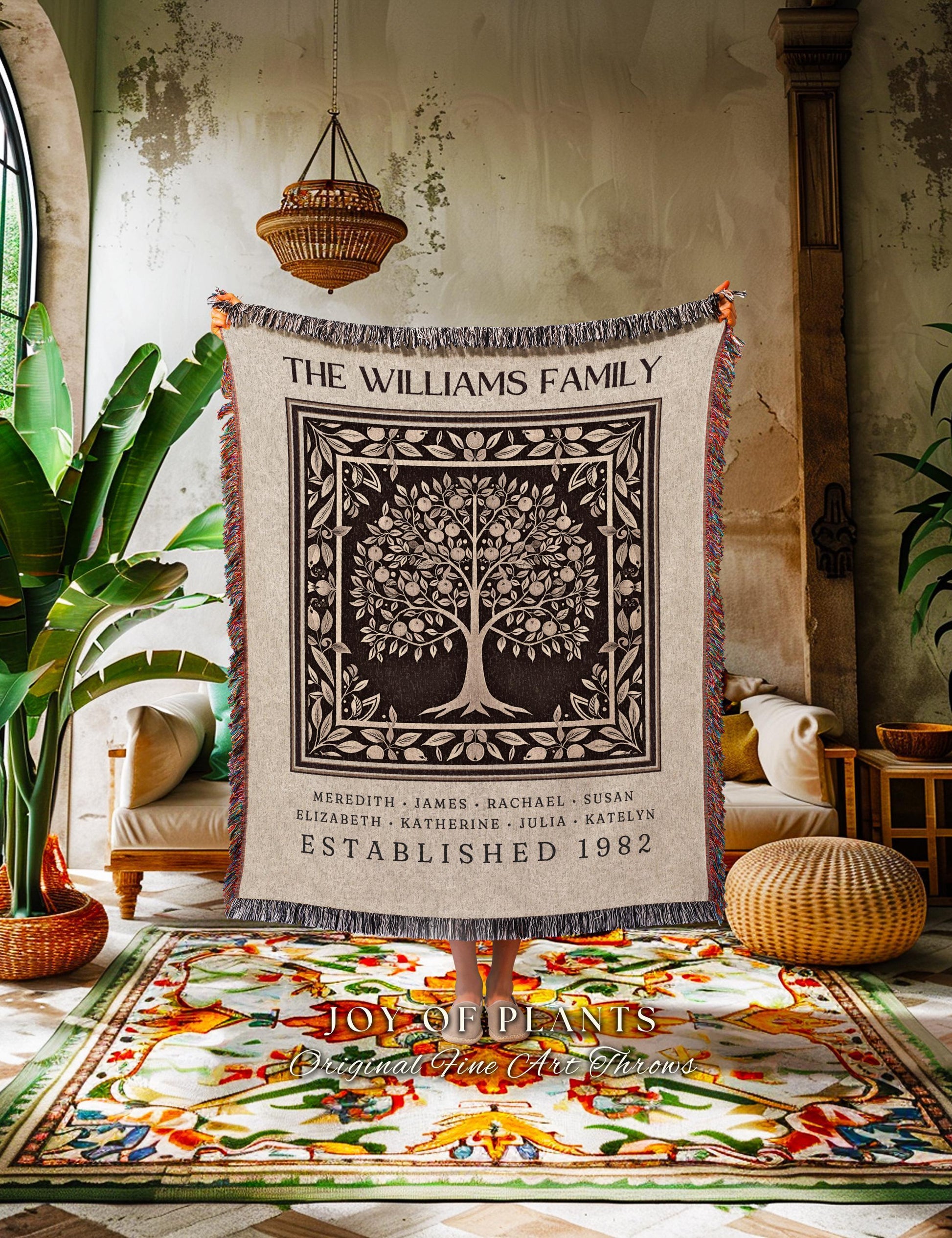 May include: A beige throw blanket with a black and white family tree design. The text "THE WILLIAMS FAMILY" is at the top, with names and "ESTABLISHED 1982" below. The blanket has a fringed edge and is displayed in a room with plants.
