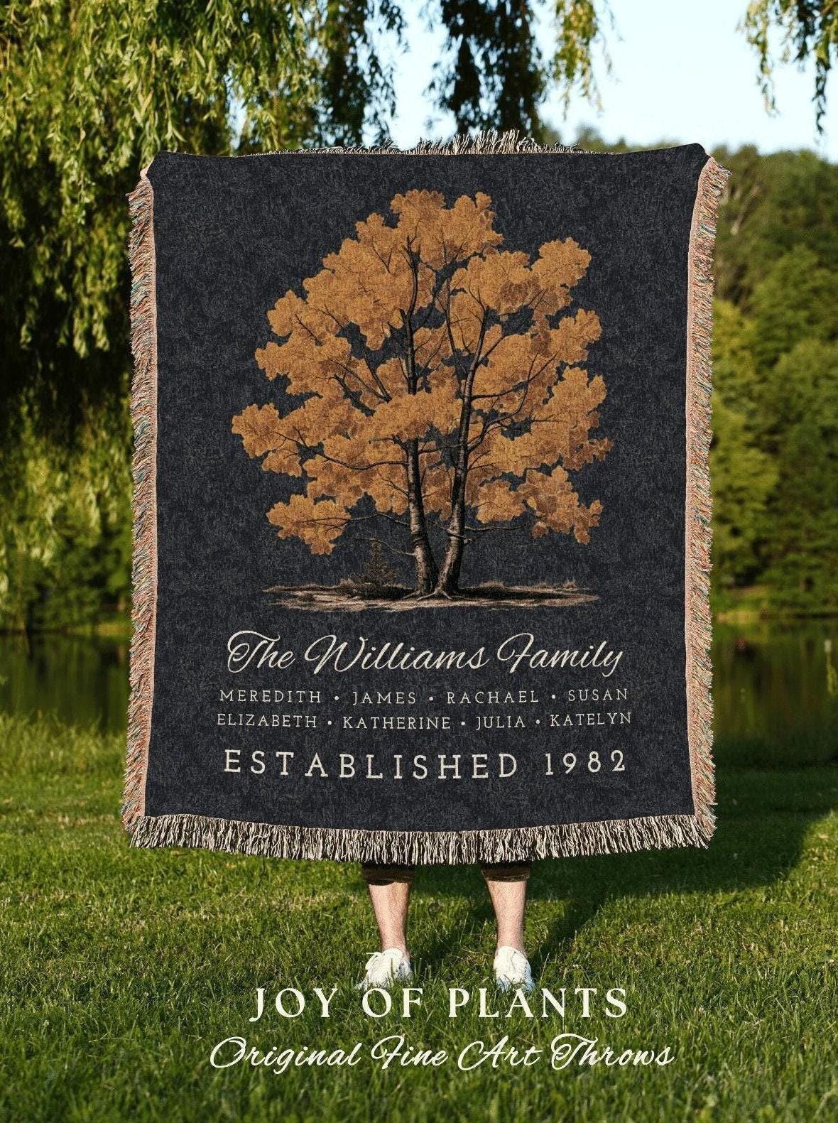 May include: A black throw blanket with a tree design in shades of brown and gold. The text "The Williams Family" is above a list of names and "ESTABLISHED 1982". The bottom reads "JOY OF PLANTS Original Fine Art Throws".