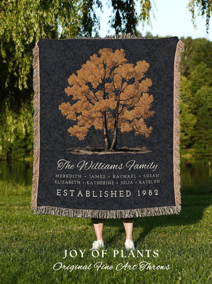 May include: A black throw blanket with a tree design in shades of brown and gold. The text "The Williams Family" is above a list of names and "ESTABLISHED 1982". The bottom reads "JOY OF PLANTS Original Fine Art Throws".