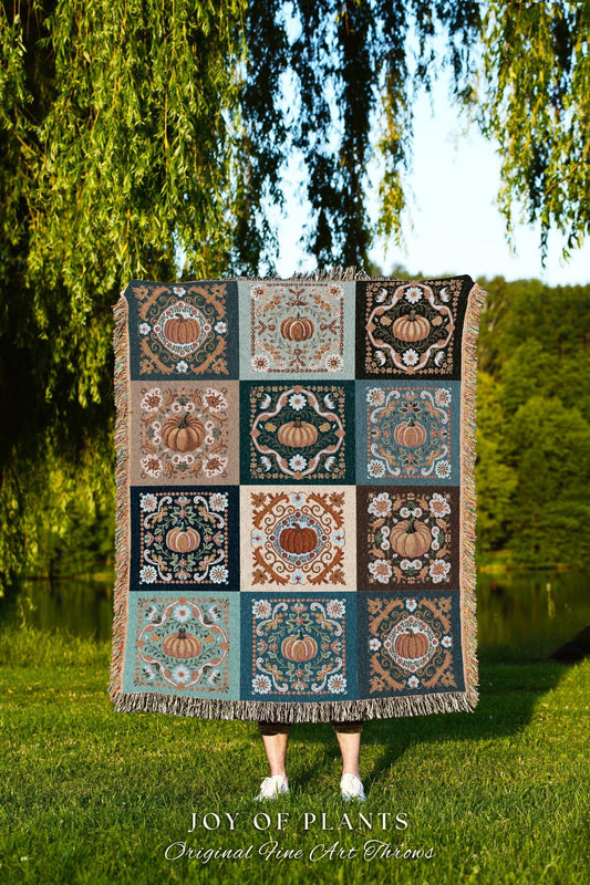 May include: A decorative throw blanket with a repeating pattern of pumpkins in squares. The blanket has a fringed edge and is held up in front of a person. The text "JOY OF PLANTS Original Fine Art Throws" is at the bottom.