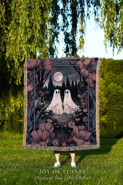 May include: A decorative throw blanket featuring a whimsical forest scene with two white ghost figures under a full moon. The blanket has a floral border in shades of purple and green, with the text "JOY OF PLANTS Original Fine Art Throws".